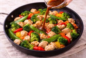 Pouring sauce over chicken and vegetables in skillet for stir fry recipe