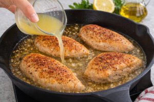 Adding garlic and lemon sauce to seared chicken breasts in a skillet for healthy lemon garlic chicken recipe