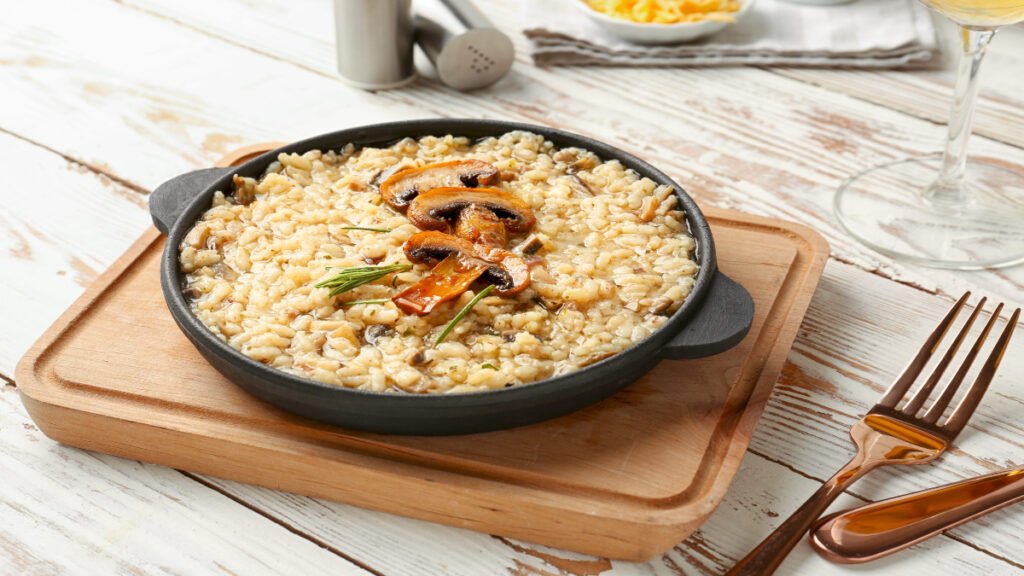 Creamy arborio rice with rich risotto texture in a skillet on a wooden cutting board
