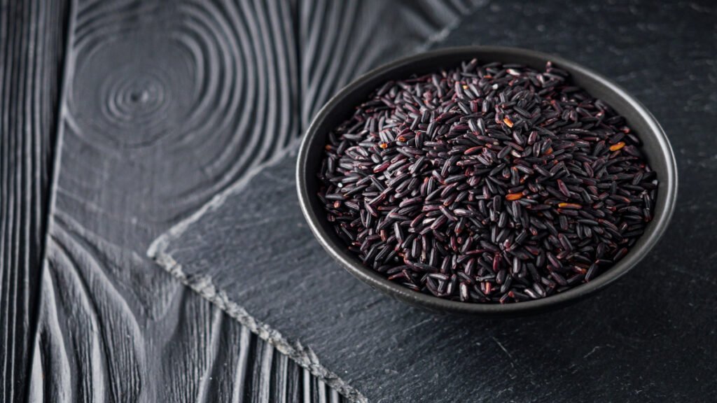 Raw black rice with deep purple color and glossy texture in a bowl