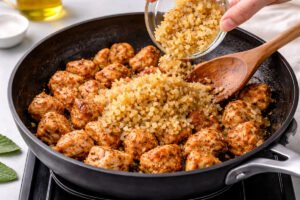 adding diced onion and garlic to cooked chicken in skillet