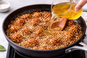 pouring chicken broth into skillet with chicken rice and seasoning