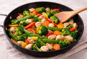 Chicken stir fry with broccoli, bell peppers, carrots and snap peas cooking in skillet