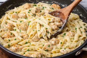 Penne pasta and chicken being mixed in creamy garlic parmesan sauce in a skillet