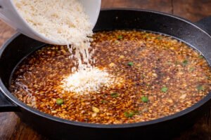 Adding rice to honey garlic sauce in skillet for chicken and rice recipe