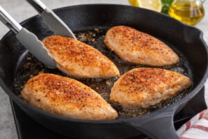 Chicken breasts searing in a skillet with olive oil for healthy lemon garlic chicken recipe