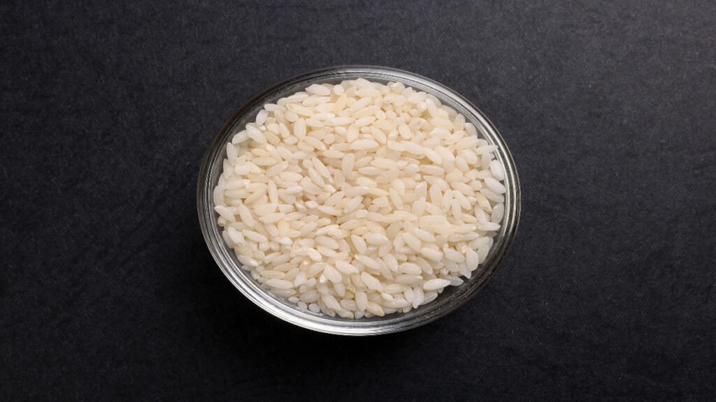 Short grain rice raw grains in a glass bowl on a black background surface