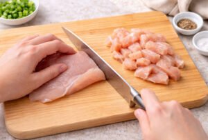 Slicing raw chicken breast into bite size pieces on cutting board for stir fry recipe