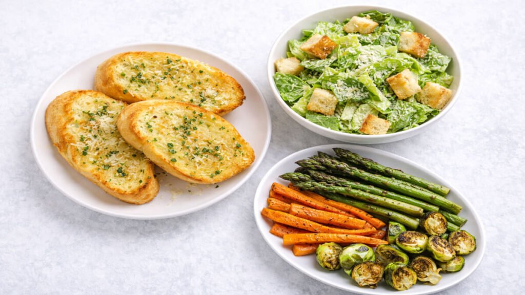 Garlic bread, Caesar salad, and roasted vegetables served as side dishes with shrimp pasta