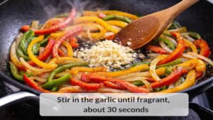 Minced garlic added to peppers and onions in a skillet for beef and pepper stir fry