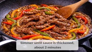 Beef peppers and onions simmering in thickened sauce in a skillet